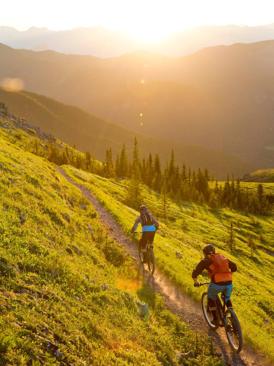 two mountain bikers riding a trail while sun in setting